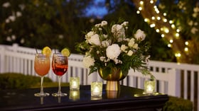 Close-up of cocktails and floral centerpiece at Lindsay Grove in Mesa, AZ with candlelight and twinkle lights in the background.