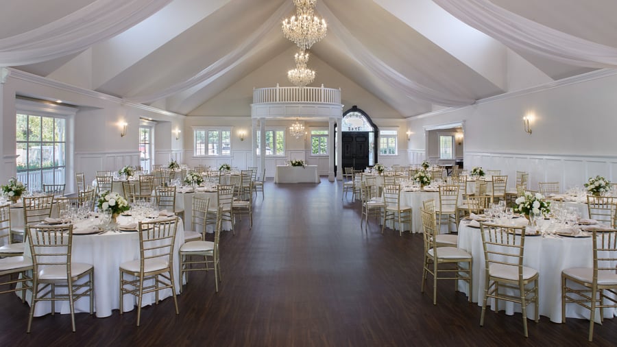 Elegant ballroom reception at Lindsay Grove Grand Hall in Mesa, AZ with chandeliers, draped ceiling fabric, round tables, and gold chiavari chairs.