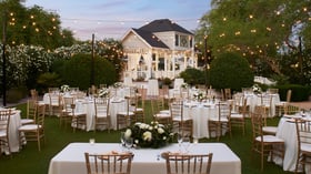 Romantic outdoor wedding reception on the brick patio at Lindsay Grove in Mesa, AZ featuring tables with white linens, gold chairs, and glowing string lights.