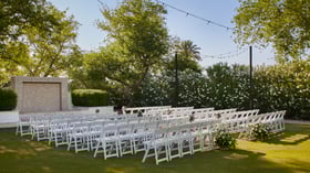 Scenic outdoor ceremony setup at Lindsay Grove in Mesa, AZ with rows of white chairs, floral arrangements, and a stone wall backdrop.