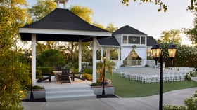 Beautiful garden wedding ceremony at Lindsay Grove in Mesa, AZ featuring a white gazebo, draped fabric, white chairs, and landscaped greenery.