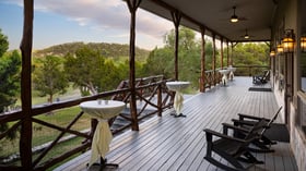 Scenic Springs porch in Helotes, Texas, set for cocktail hour with high-top tables, rocking chairs, and scenic hill country views.