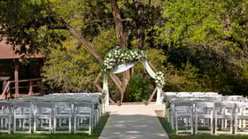 Close-up of Scenic Springs wedding ceremony setup in Helotes, Texas, with a wooden hexagon arch draped in white fabric and greenery.