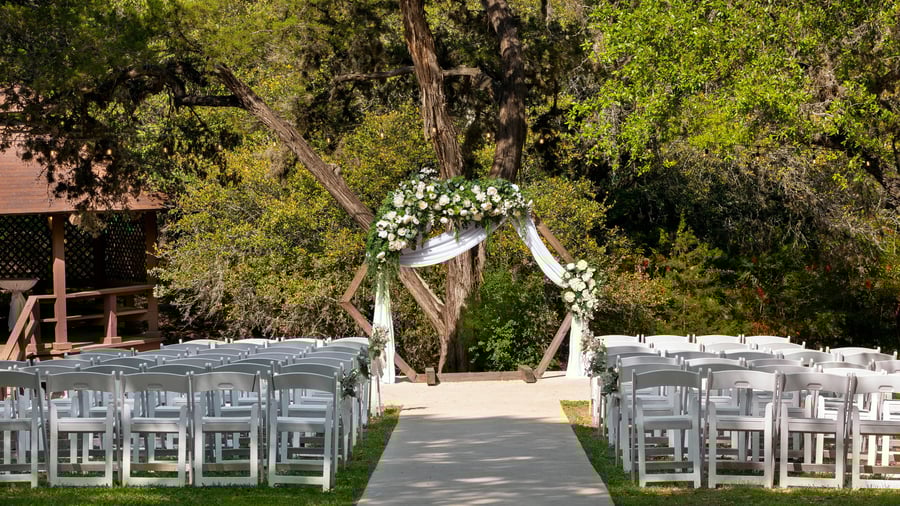 Close-up of Scenic Springs wedding ceremony setup in Helotes, Texas, with a wooden hexagon arch draped in white fabric and greenery.