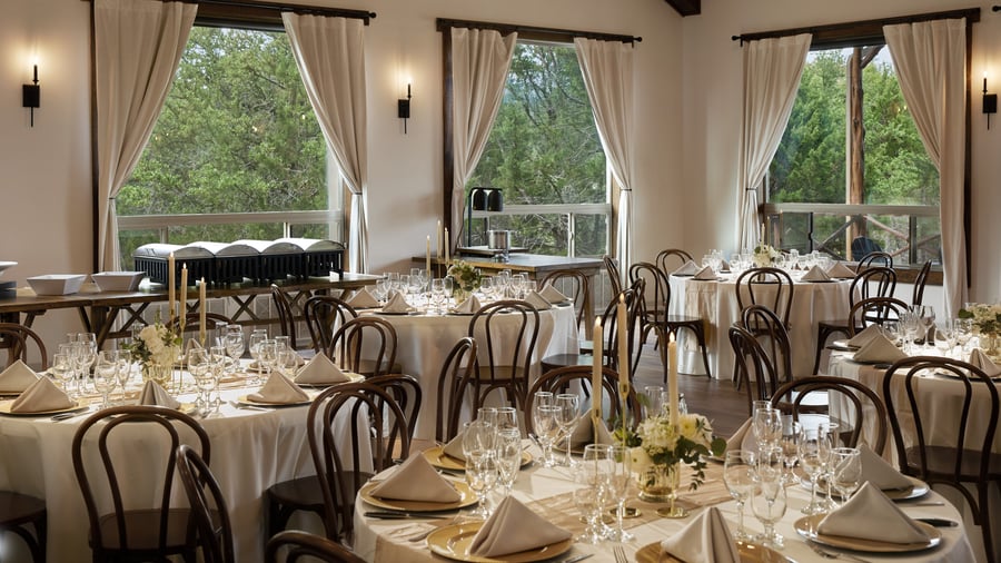 Scenic Springs reception hall in Helotes, Texas, with gold table settings, elegant floral centerpieces, and large windows overlooking greenery.