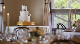 Elegant three-tier wedding cake on gold stand in Scenic Springs ballroom reception space in Helotes, Texas.