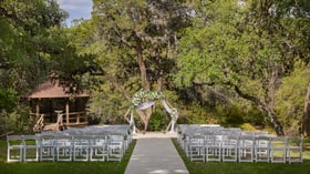 Outdoor ceremony space at Scenic Springs in Helotes, Texas, with floral hexagon arch, white chairs, and oak trees.