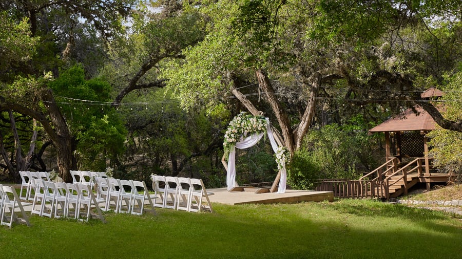 Scenic Springs outdoor wedding ceremony site with a floral arch, white chairs, and rustic gazebo in Helotes, Texas.