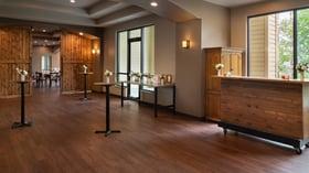 Elegant cocktail hour setup at The Pines featuring barn-style wooden doors, tall bistro tables with floral vases, and large windows overlooking the forest.