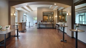 Stylish cocktail lounge at The Pines with wood flooring, mirrors, tall tables with white flowers, and natural light pouring through large windows.