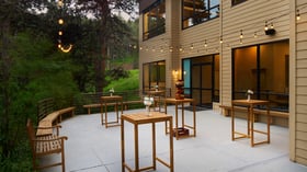 Outdoor cocktail hour patio at The Pines with tall wooden tables, string lights, and forest surroundings offering a relaxed mountain vibe.
