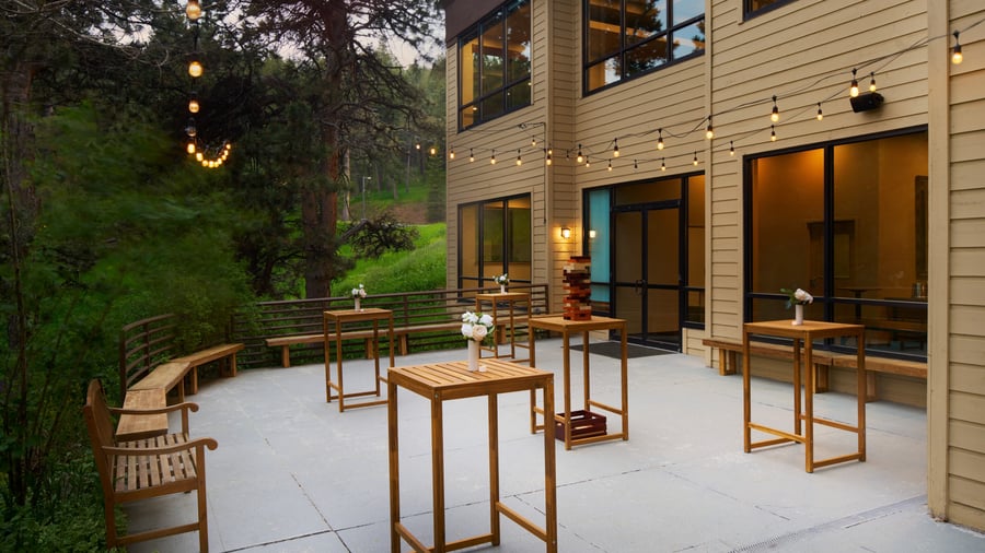 Outdoor cocktail hour patio at The Pines with tall wooden tables, string lights, and forest surroundings offering a relaxed mountain vibe.