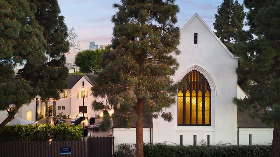 Exterior view of The Sanctuary Cathedral in Long Beach at dusk, featuring illuminated stained glass and courtyard lighting.