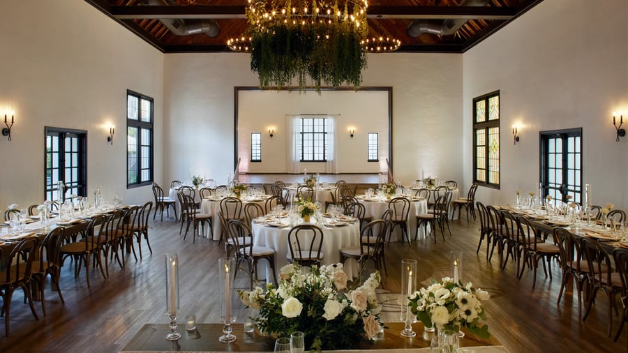 The Grand Hall at The Sanctuary in Long Beach set for a wedding reception with round tables, greenery chandelier, and white florals