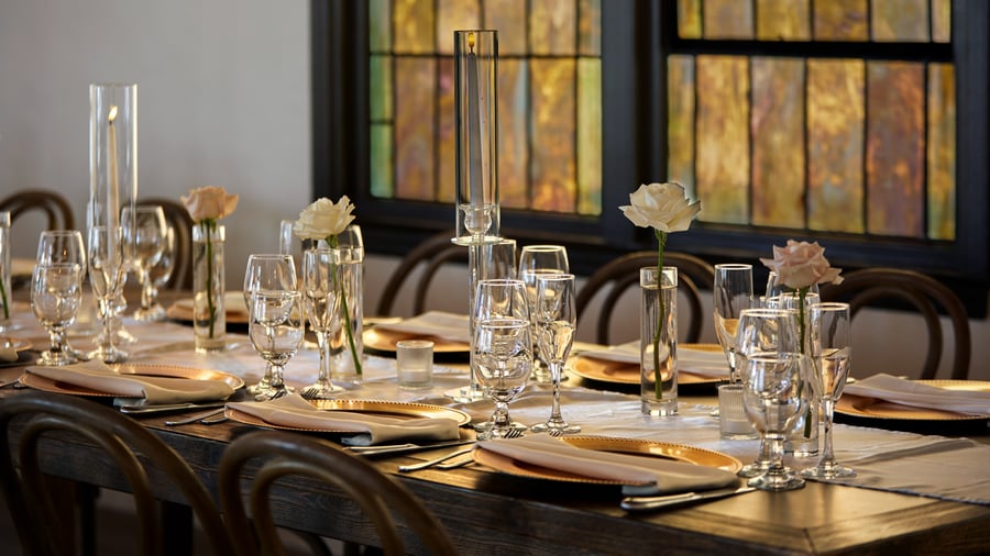 Elegant wedding table setting in The Sanctuary’s Grand Hall, Long Beach, with gold chargers, glassware, and single rose centerpieces.