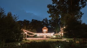 Charming farm-style wedding venue at Alexander Homestead illuminated at twilight with string lights and ceremony seating.