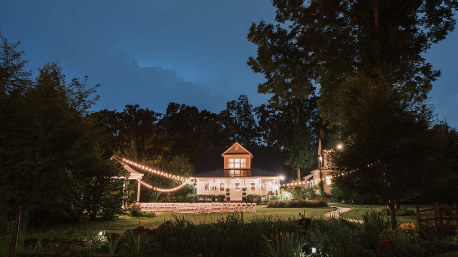 Charming farm-style wedding venue at Alexander Homestead illuminated at twilight with string lights and ceremony seating.