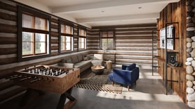 Contemporary lounge area at Casa del Rio Fresno featuring rustic log walls, large windows, foosball table, sectional gray sofa, blue accent chair, wooden coffee tables, geometric area rug, and river stone accents for casual gathering spaces.