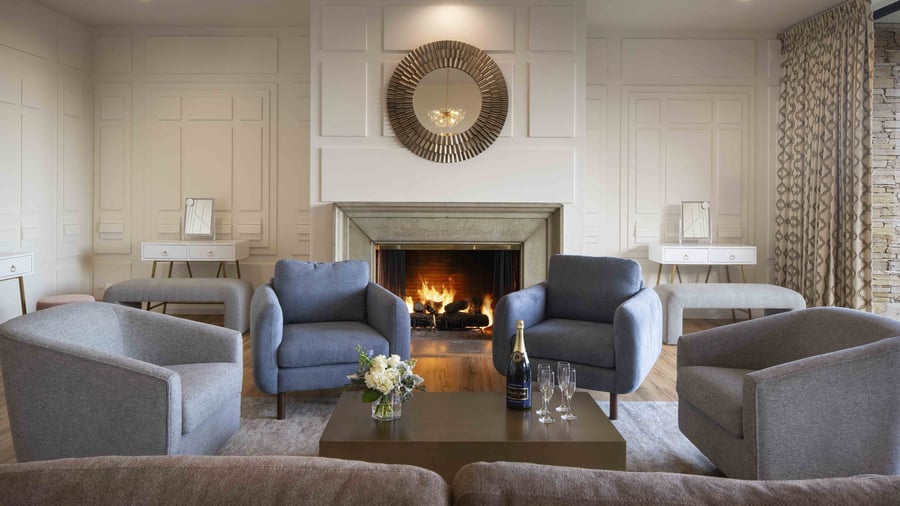 Luxurious pre-function lounge featuring roaring stone fireplace, designer furnishings in soothing gray tones, and contemporary accents - ideal for intimate gatherings and wedding party relaxation
