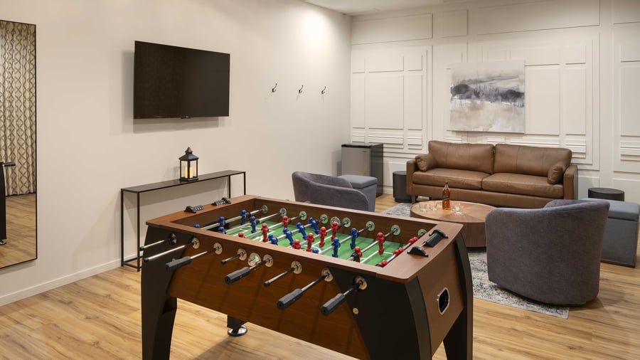 Modern get-ready lounge featuring entertainment amenities including professional foosball table, flat-screen TV, leather sofas, and stylish decor - providing the perfect pre-ceremony relaxation space for the wedding party