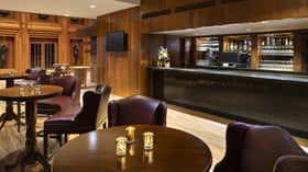 Luxurious clubhouse lounge featuring rich wood paneling, burgundy leather seating, and elegant bar with premium spirits display - perfect for sophisticated pre-wedding gatherings and intimate cocktail receptions