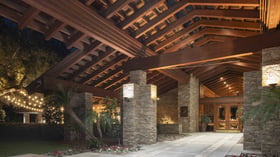 Architectural marvel entrance pavilion with dramatic exposed timber beams, illuminated stacked stone columns, and ambient lighting creating an unforgettable arrival experience for wedding guests