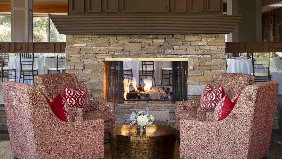 Elegant mountain lodge fireplace lounge featuring rich textiles, comfortable seating in warm burgundy tones, and pass-through stone fireplace - creating a cozy atmosphere for intimate wedding gatherings