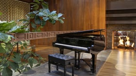 Artistic grand piano installation nestled among lush fiddle leaf figs with glowing fireplace backdrop, offering sophisticated ambiance for cocktail hour musical performances and reception entertainment