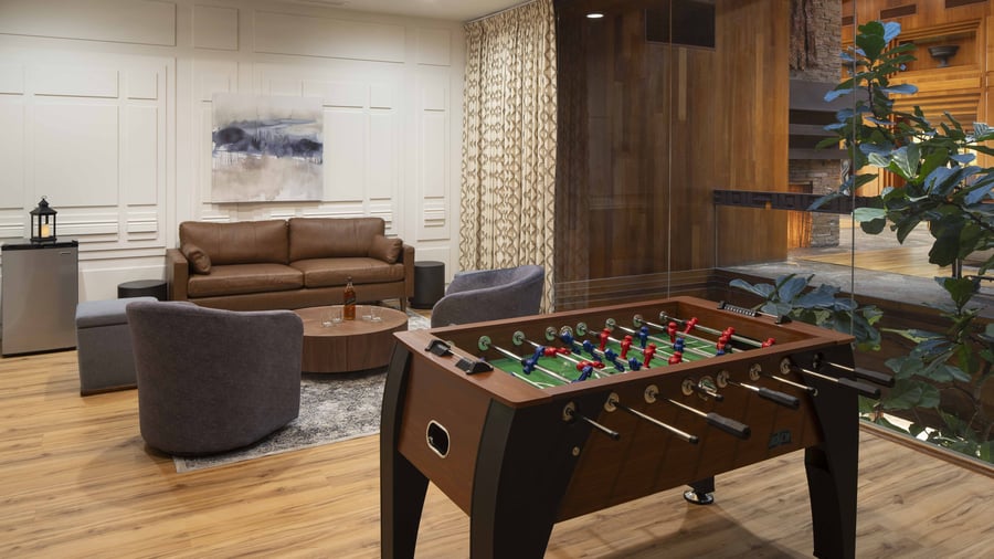 Contemporary get ready lounge featuring leather sofa, premium entertainment options including professional foosball table, and custom artwork - providing a stylish retreat for the wedding party