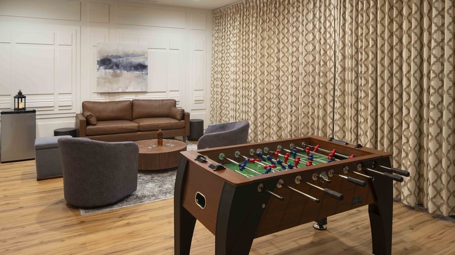 Versatile entertainment lounge featuring premium foosball table, comfortable seating areas, and custom wall treatments - perfect for rehearsal dinners and guest gatherings