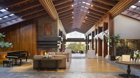 Magnificent mountain lodge great room featuring dramatic vaulted ceilings with exposed beams, floor-to-ceiling windows framing valley views, luxurious seating areas, and grand piano - perfect for cocktail receptions and intimate gatherings