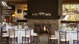 Elegant fireplace reception space with natural stone hearth, dramatic ceilings, artful lighting, and impeccably set dining tables with fresh floral centerpieces, creating a warm and inviting atmosphere for memorable wedding celebrations