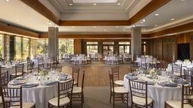 Expansive ballroom with warm wood architectural details, natural light flooding through floor-to-ceiling windows, and versatile open floor plan perfect for grand receptions of up to 200 guests with dedicated dance floor area