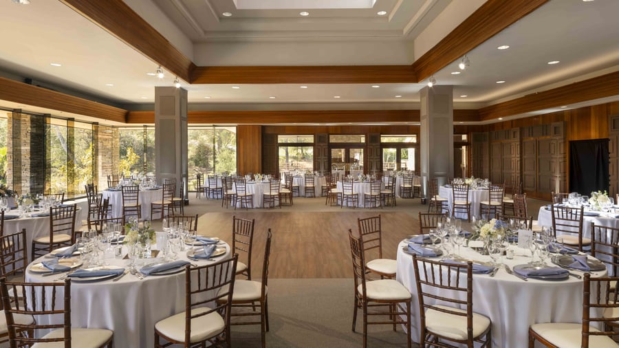 Expansive ballroom with warm wood architectural details, natural light flooding through floor-to-ceiling windows, and versatile open floor plan perfect for grand receptions of up to 200 guests with dedicated dance floor area