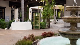 Charming event welcome table setup at Fallbrook Estate Wedgewood Events with decorative fountain, gold geometric backdrop, covered patio with string lights for corporate events and private celebrations