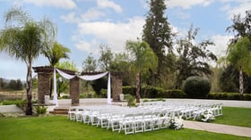 Picturesque garden event ceremony at Fallbrook Estate Wedgewood Events with stone archway, white draping, white chairs on manicured lawn for outdoor corporate events and celebrations