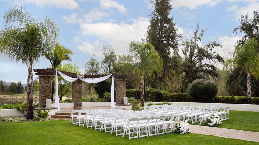Picturesque garden event ceremony at Fallbrook Estate Wedgewood Events with stone archway, white draping, white chairs on manicured lawn for outdoor corporate events and celebrations