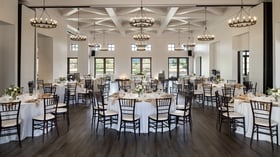 Sophisticated indoor event reception space at Fallbrook Estate Wedgewood Events featuring exposed beam ceiling, wrought iron chandeliers, round tables with chairs and panoramic windows for corporate meetings and private parties