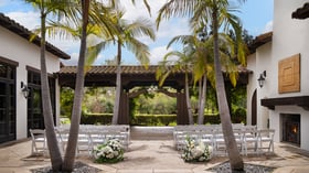 Charming courtyard event space at Fallbrook Estate Fallbrook California with white folding chairs, tropical palm trees, Spanish colonial architecture and outdoor fireplace for small gatherings and celebrations