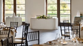 Beautiful VIP event table setup at Fallbrook Estate Wedgewood Events with white floral garland, elegant chairs, cake table and panoramic windows overlooking golf course for executive events in Fallbrook California