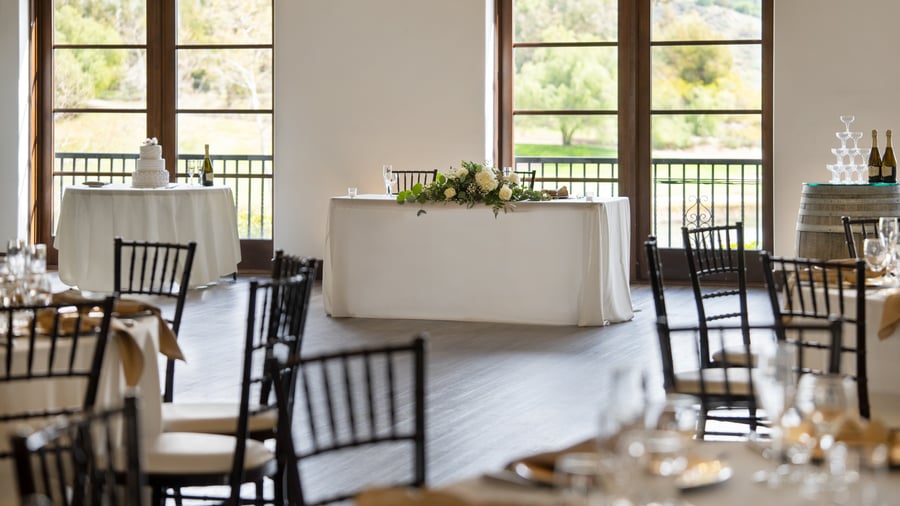 Beautiful VIP event table setup at Fallbrook Estate Wedgewood Events with white floral garland, elegant chairs, cake table and panoramic windows overlooking golf course for executive events in Fallbrook California