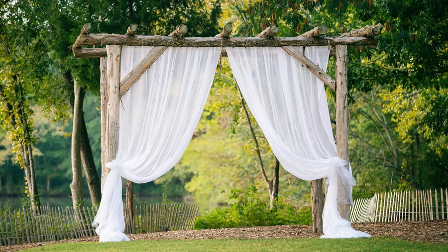 Natural wood arbor with white drapery at Riverwood Manor's lakeside venue space, perfect for outdoor ceremonies, presentations, and special events in a scenic woodland setting - Ken Thomas Photography