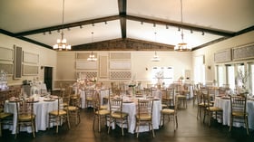 Interior view of Riverwood Manor's Grand Hall featuring vaulted ceilings with wooden beams, chandeliers, elegant table settings with white linens and gold chiavari chairs for corporate events and social gatherings - Ken Thomas Photography