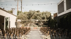 Outdoor ceremony setup in olive garden courtyard with gold metal chairs and aisle florals at Orange County venue