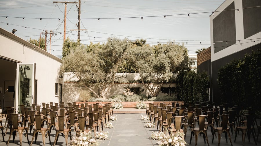 Outdoor ceremony setup in olive garden courtyard with gold metal chairs and aisle florals at Orange County venue