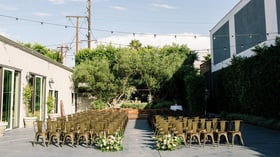 Sun-drenched courtyard ceremony space at The Harper with string lights, olive trees, and metal chairs in champagne finish